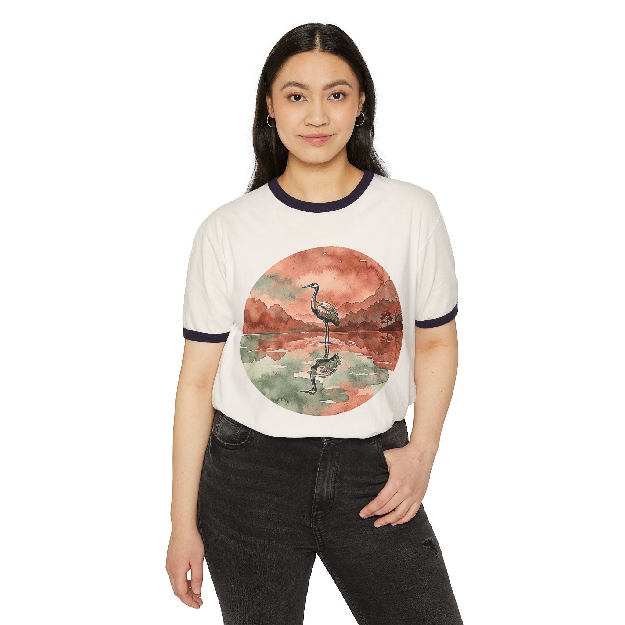 A woman wearing a Chromatic retro ringer tee featuring a watercolor crane reflecting in a pond on a white background.