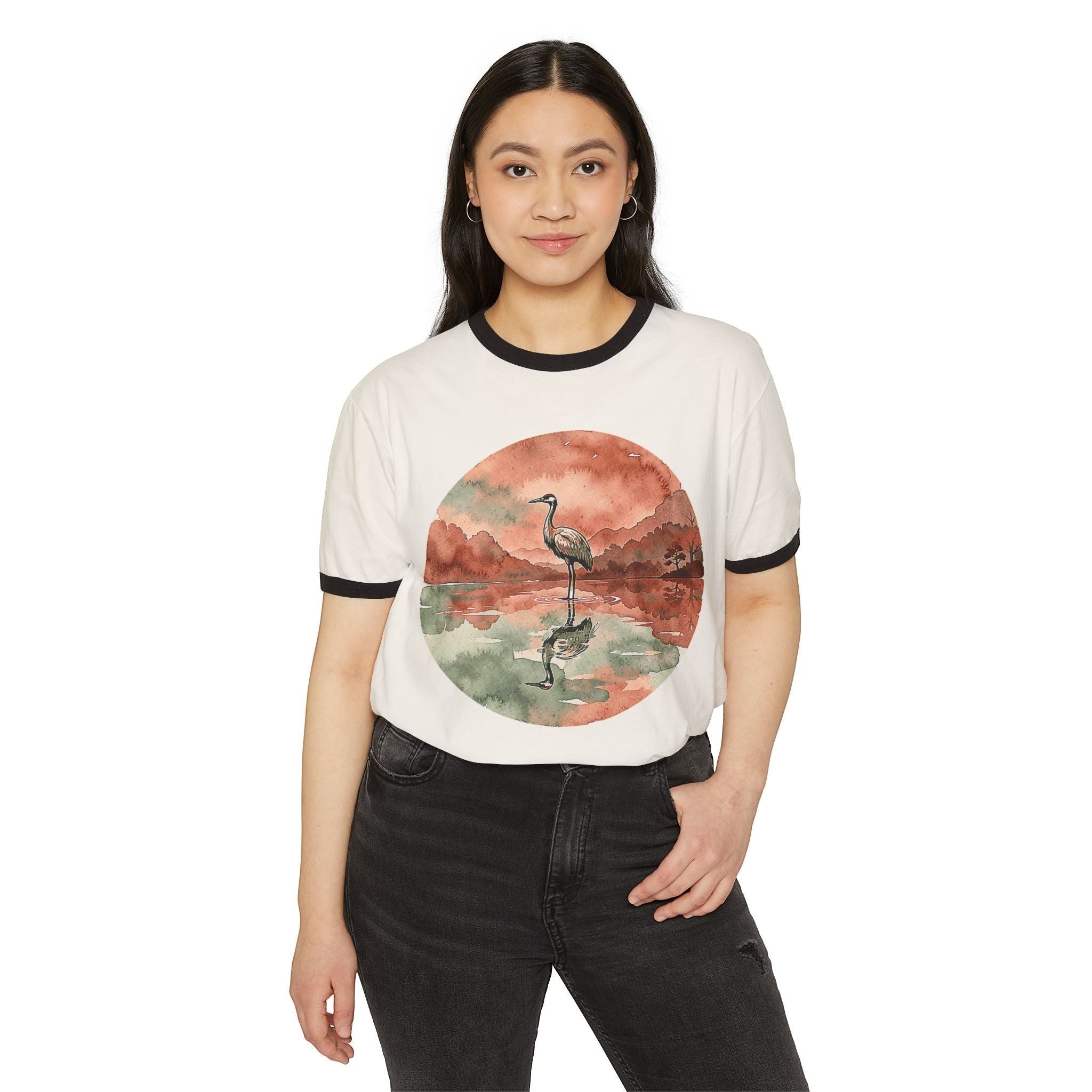 A woman wearing a Chromatic white ringer tee with a watercolor crane reflecting in a pond graphic, retro style.